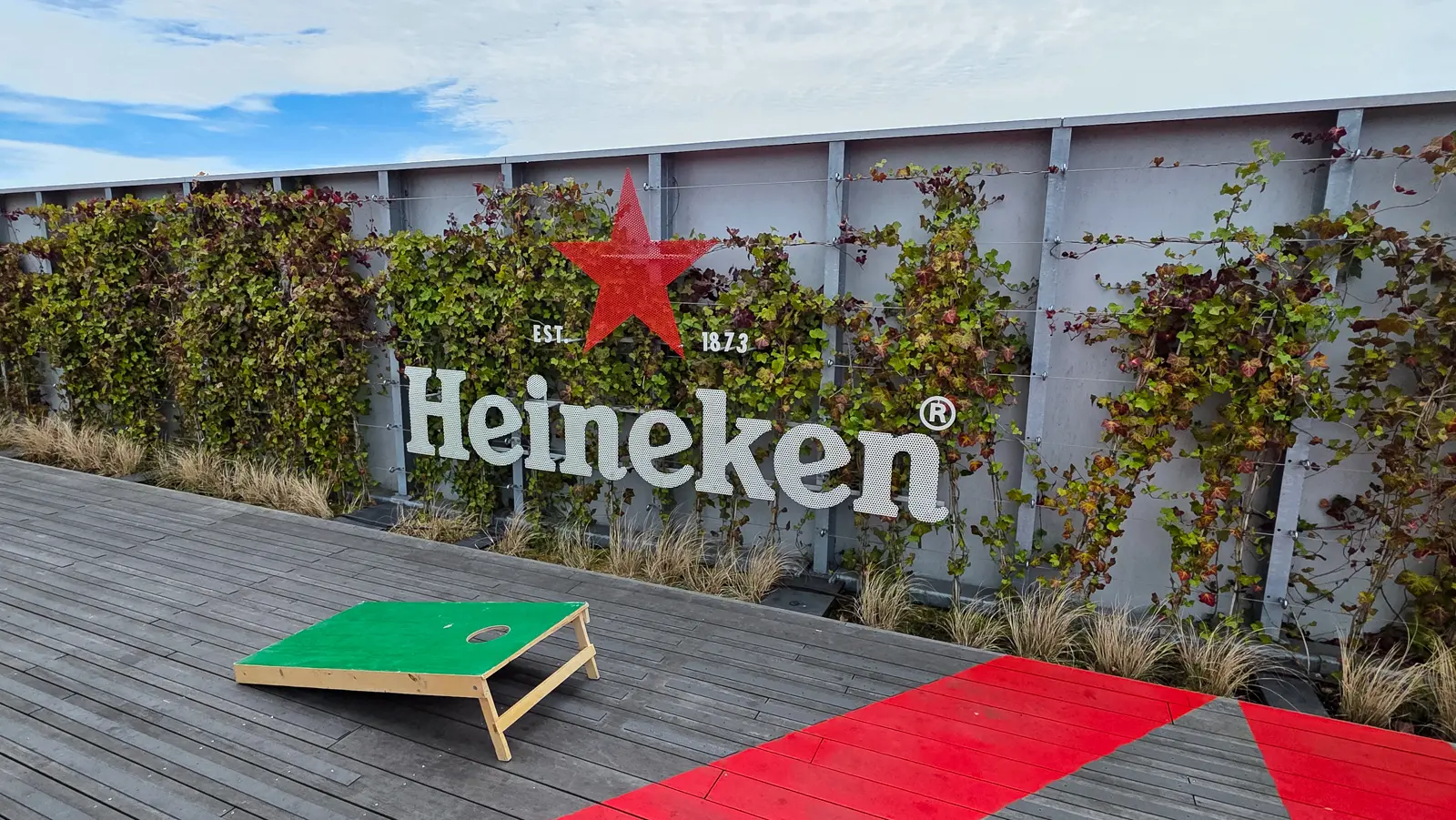 Heineken sign mounted on an ivy-covered wall on the rooftop terrace in Amsterdam, with a cornhole board on the decking in front of it