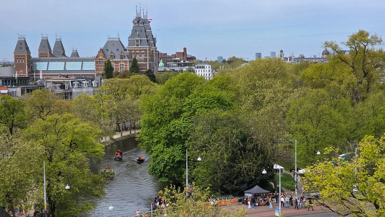 View from the Heineken rooftop in Amsterdam towards the Rijksmuseum, with boats of people in orange on the canal below on King’s Day