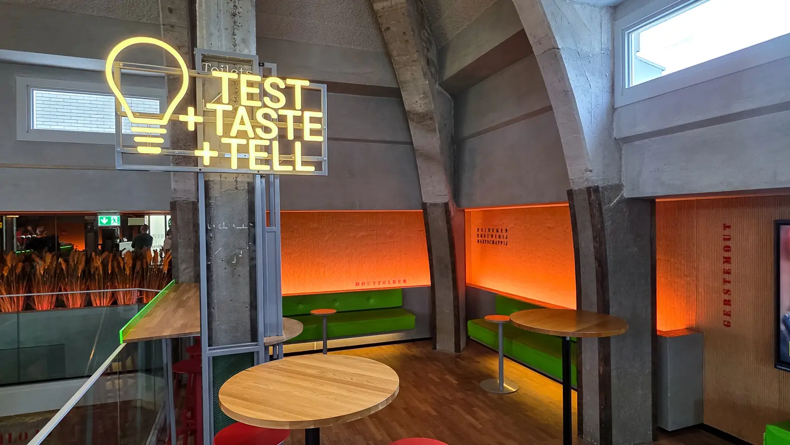 Malt attic seating at the Heineken Experience, Amsterdam, with orange-lit alcoves, green benches and red lettering on the wall