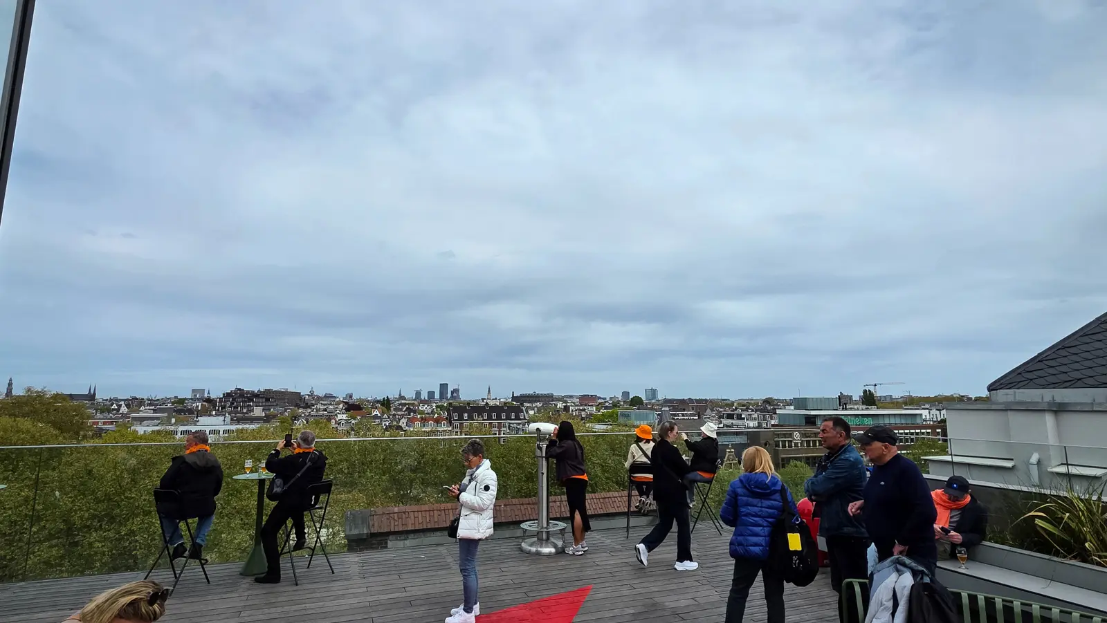 Visitors at the rooftop railing of the Heineken Experience, Amsterdam, with a telescope and the city skyline beyond