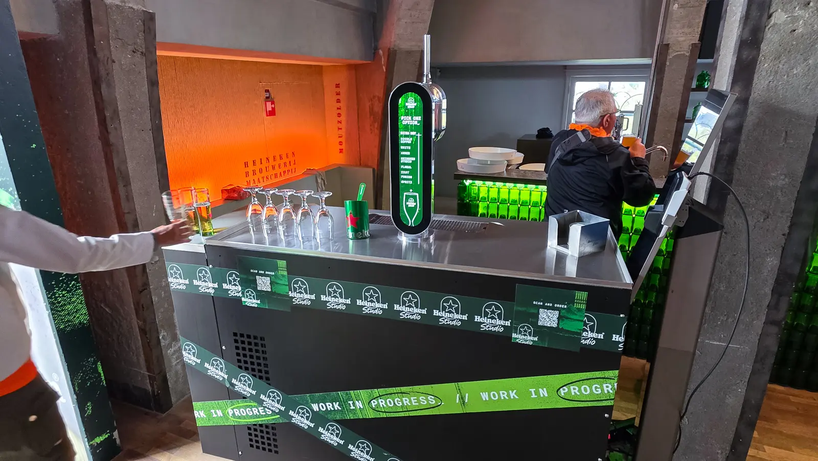 Heineken Studio bar at the Heineken Experience rooftop in Amsterdam, its tap listing eight options above a counter wrapped in branded tape