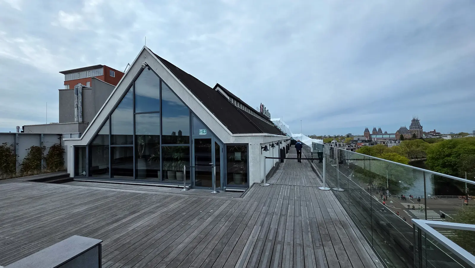 Timber decking beside a gabled glass-fronted structure on the Heineken Experience roof, Amsterdam, with the Rijksmuseum beyond