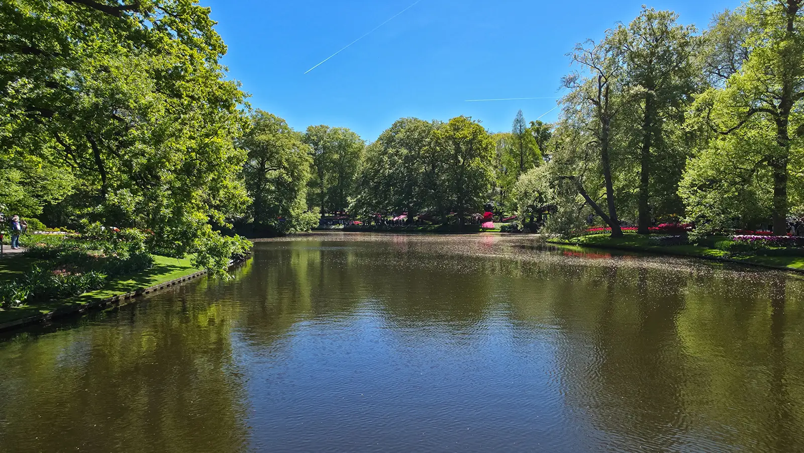 The wide main lake at Keukenhof, Lisse, reflecting trees and blue sky, with flower beds along both banks in the distance