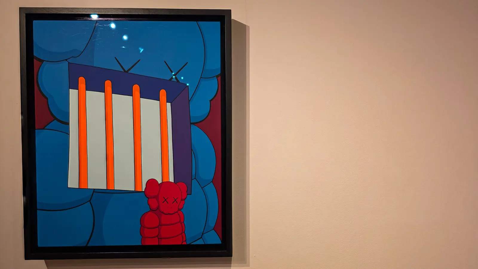 Lonely Thoughts by KAWS, a small red figure crouched behind four bright orange bars on a white panel with a larger blue figure filling the background, framed behind glass, Moco Museum