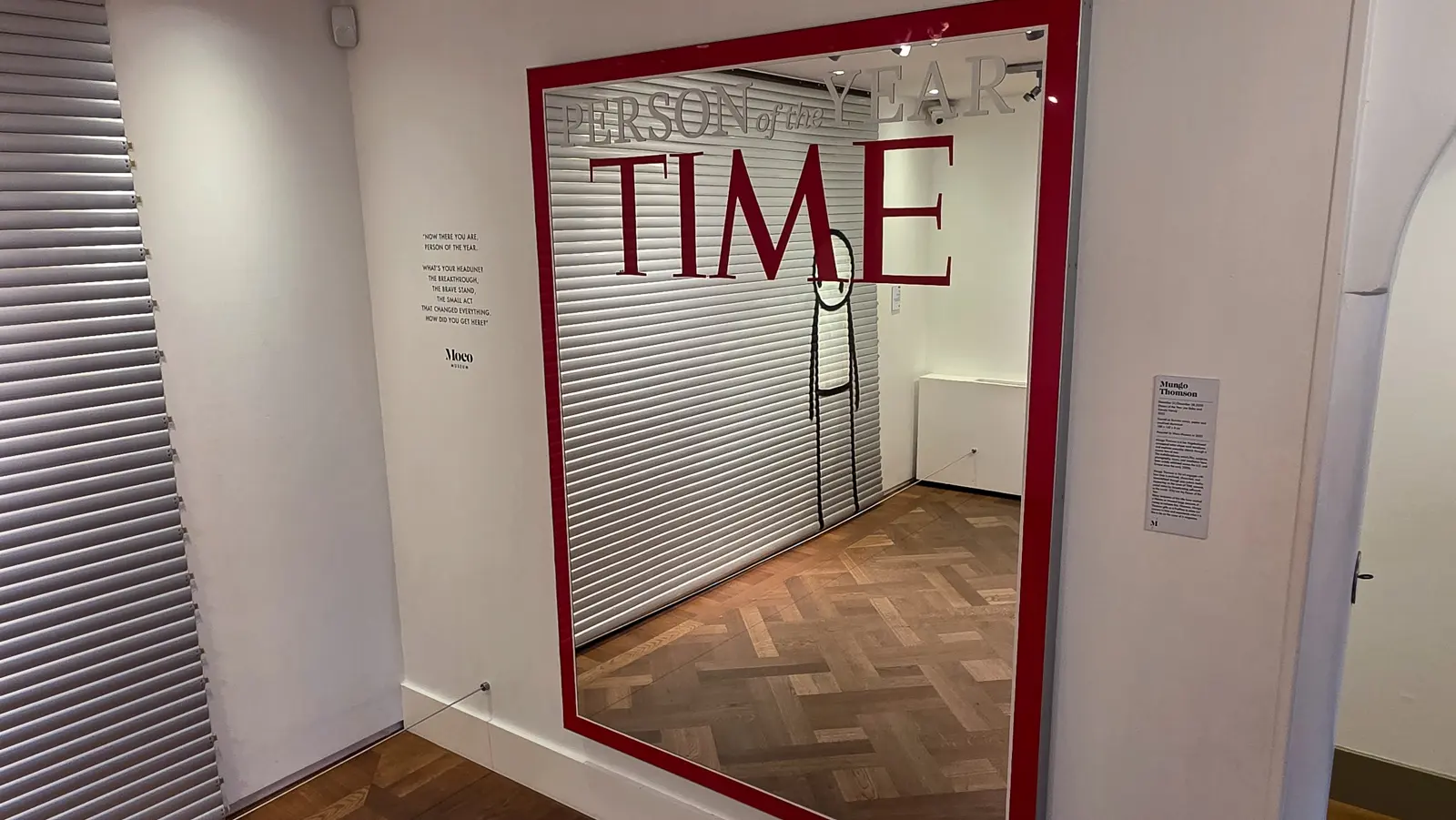 Mungo Thomson's TIME magazine Person of the Year mirror at the Moco Museum, reflecting the herringbone-floor room with a stick figure drawn on the glass