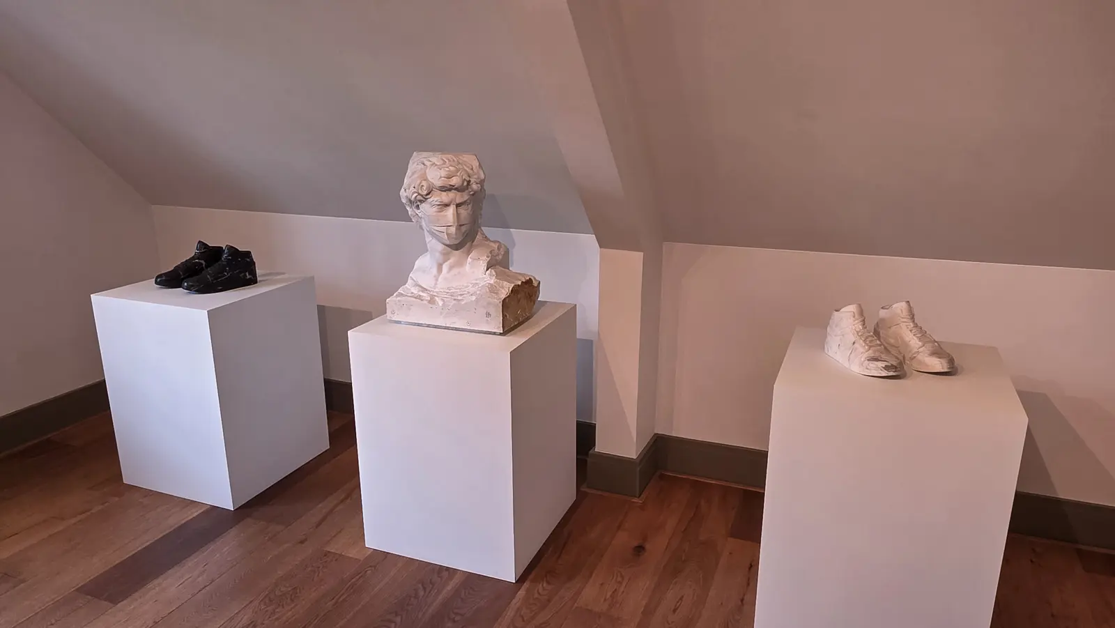 David-19 by Tonarelli, a marble bust of Michelangelo's David wearing a carved surgical mask, deliberately unfinished, between two marble shoe sculptures, Moco Museum, Amsterdam