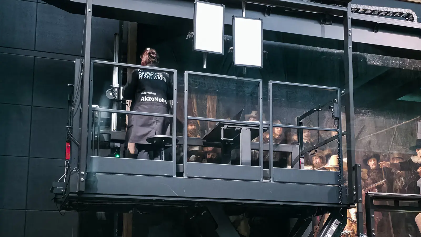 Conservator on the raised platform beside the Night Watch at the Rijksmuseum, Amsterdam, wearing an Operation Night Watch apron