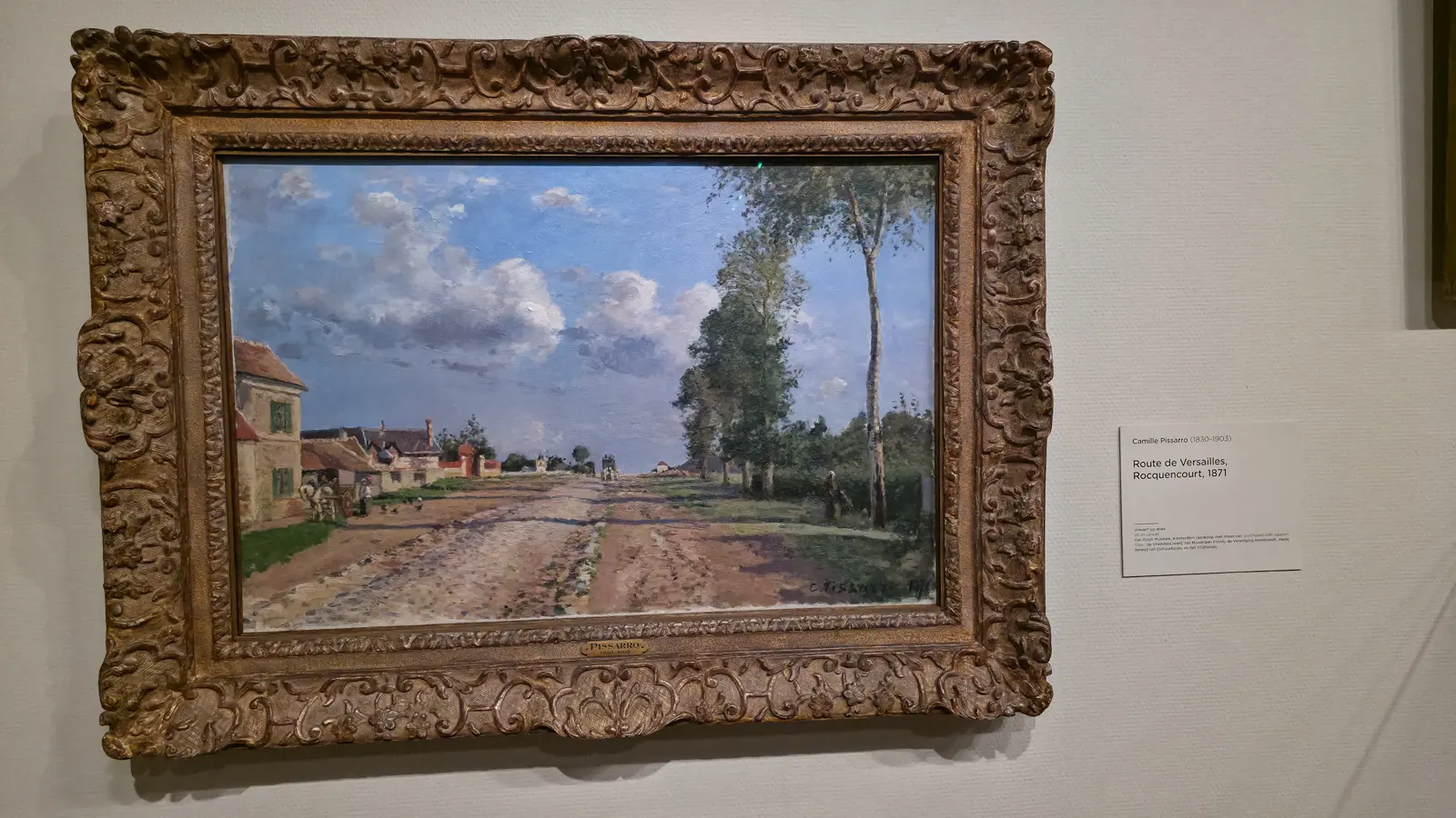 Camille Pissarro's Route de Versailles, Rocquencourt (1871) at the Van Gogh Museum, a long country road under white clouds with houses and trees