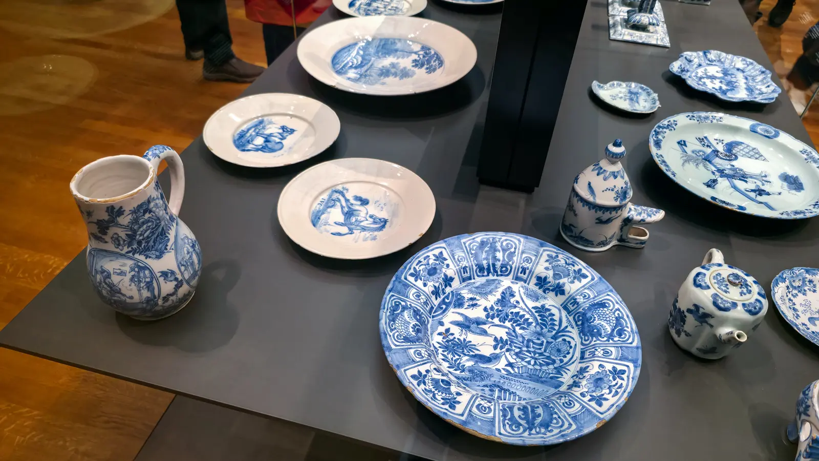 Delft blue and white jug, plates and teapot arranged on a museum table, Rijksmuseum, Amsterdam