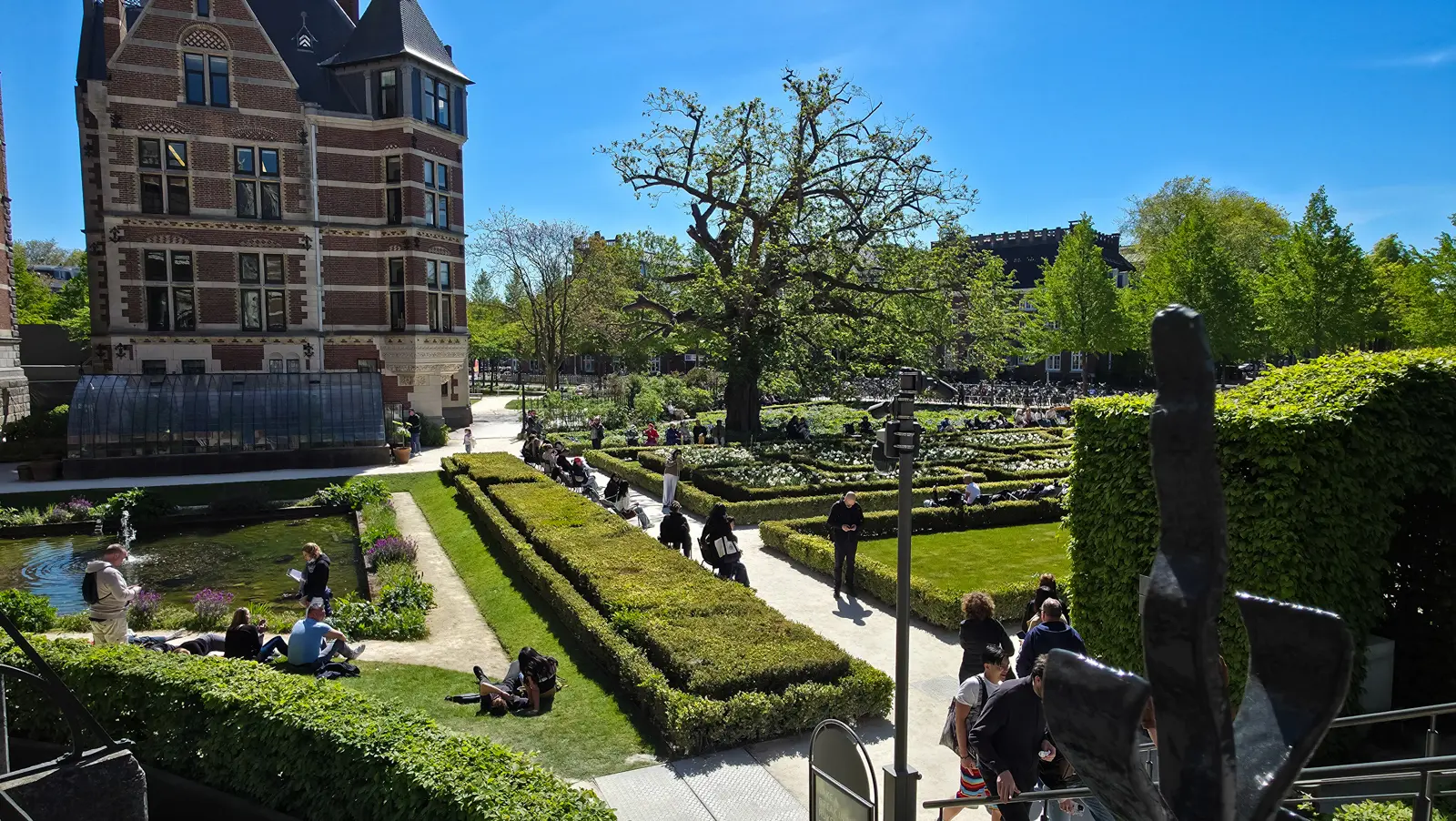 Elevated view over the Rijksmuseum gardens on a sunny day, with people seated on the grass beside the sunken pond