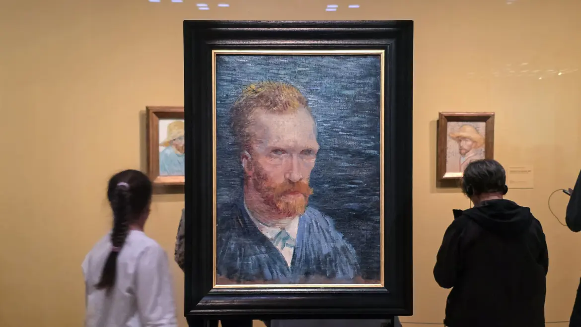Visitors either side of Van Gogh's blue 1887 self-portrait in a black frame on a freestanding stand, Van Gogh Museum, Amsterdam