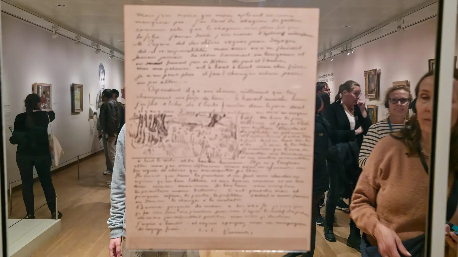 A Van Gogh letter displayed on glass at the Van Gogh Museum, dense brown-ink handwriting with a landscape sketch of a field and trees drawn into the middle of the page