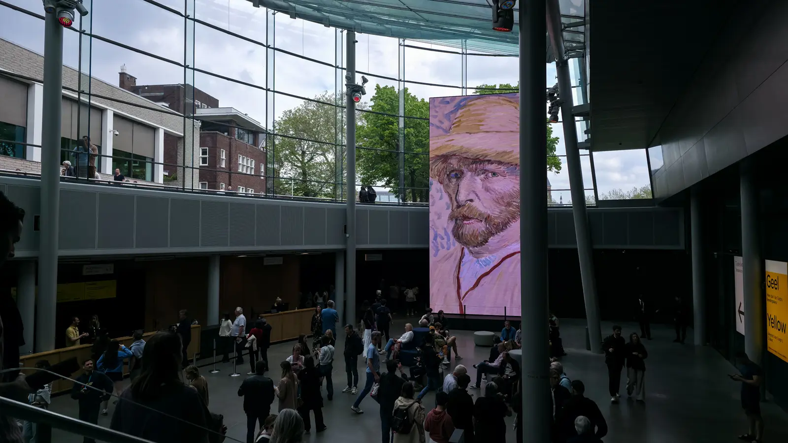 Entrance hall of the Van Gogh Museum, Amsterdam, with a Van Gogh self-portrait on a tall screen and visitors gathered below the glass roof