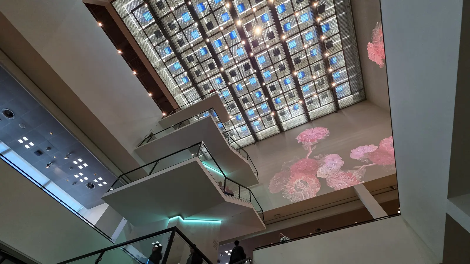 Glass entrance hall at the Van Gogh Museum, Amsterdam, looking up at the skylight grid past staircases and a floral projection