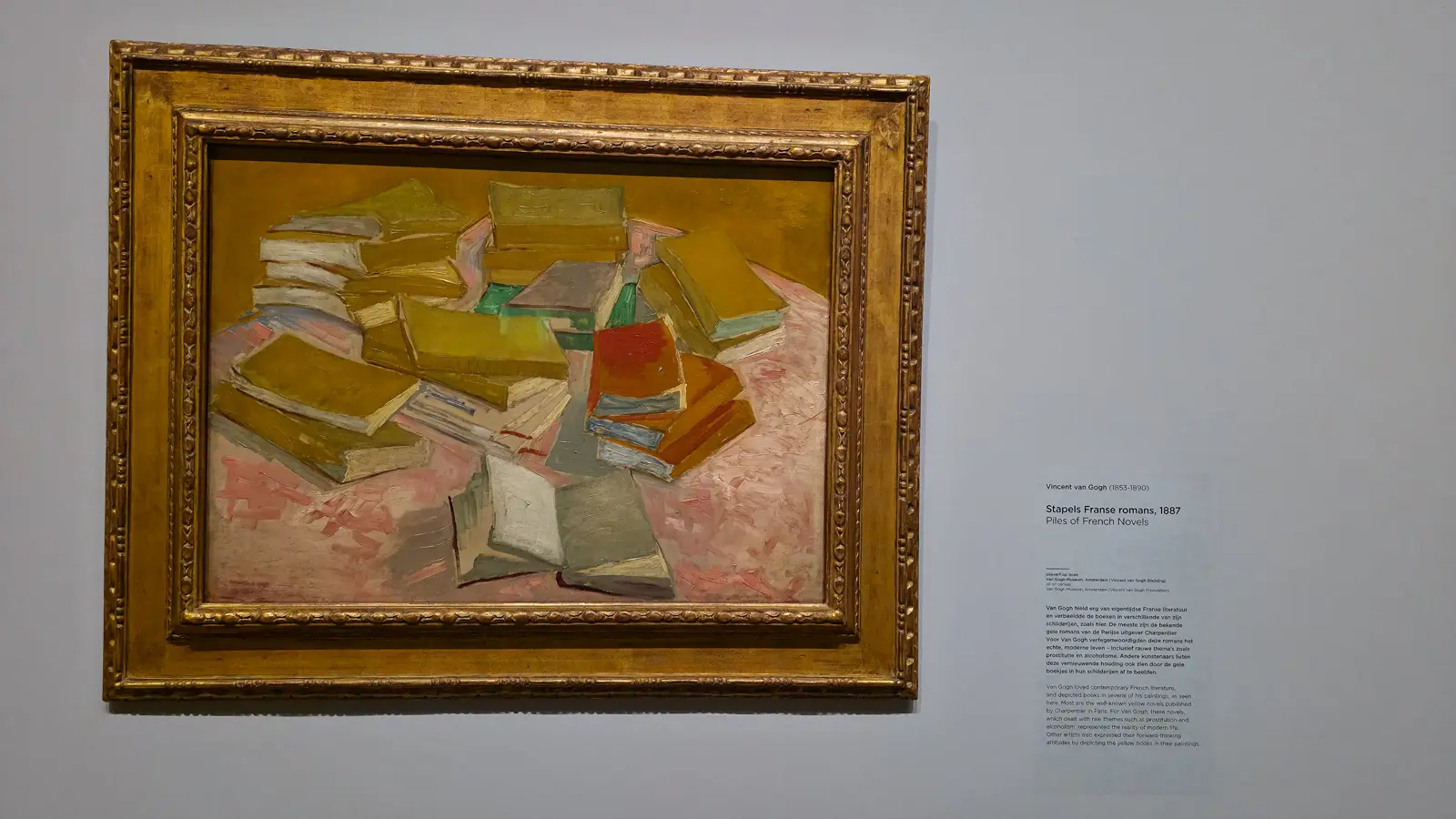 Van Gogh's Piles of French Novels (1887), stacks of yellow and red paperbacks spread across a pink surface, in a gilt frame at the Van Gogh Museum
