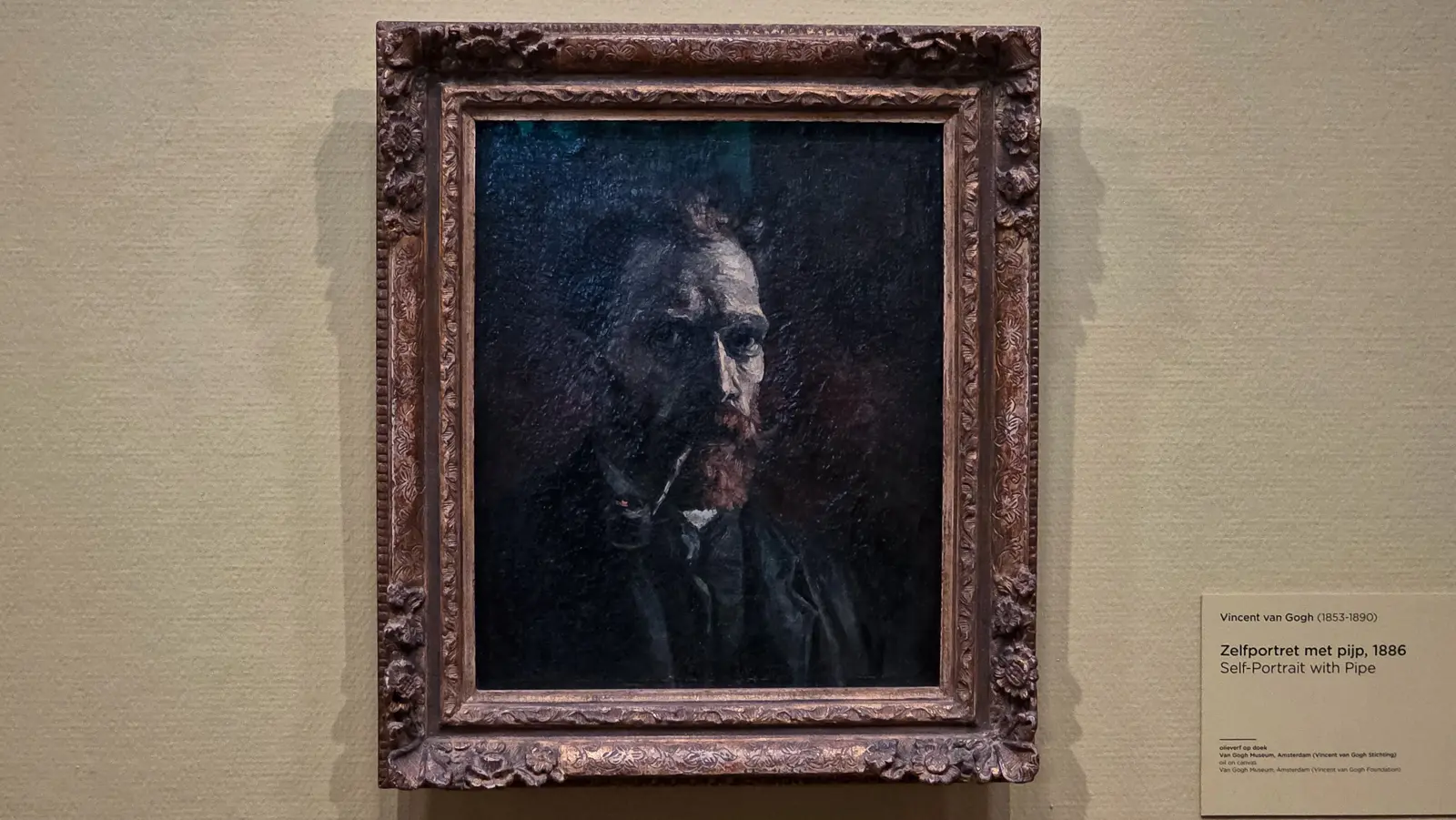 Self-Portrait with Pipe, 1886, a near-black canvas in a carved gilt frame with its wall label, Van Gogh Museum, Amsterdam