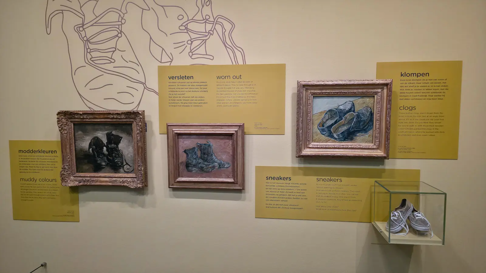 Three Van Gogh shoe paintings from 1886 to 1889 displayed with yellow explanatory panels and a visitor's own trainers in a glass case, Van Gogh Museum