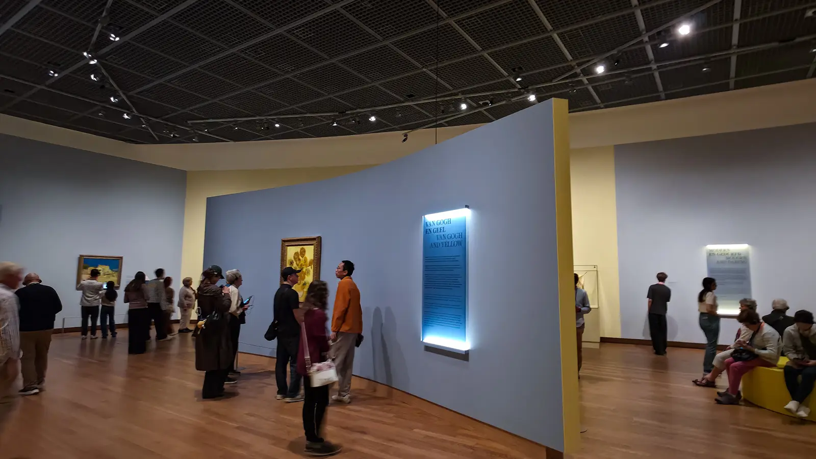Visitors in the Yellow exhibition at the Van Gogh Museum, with the Sunflowers and The Yellow House on curved grey walls and a backlit intro panel