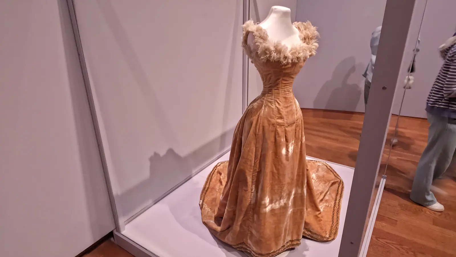 A pale gold velvet evening gown with a feathered neckline and a long train, on a mannequin in a glass case in the Yellow exhibition at the Van Gogh Museum