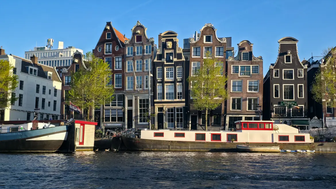 Gabled canal houses on the Amstel in Amsterdam, with a white houseboat with red window frames moored below