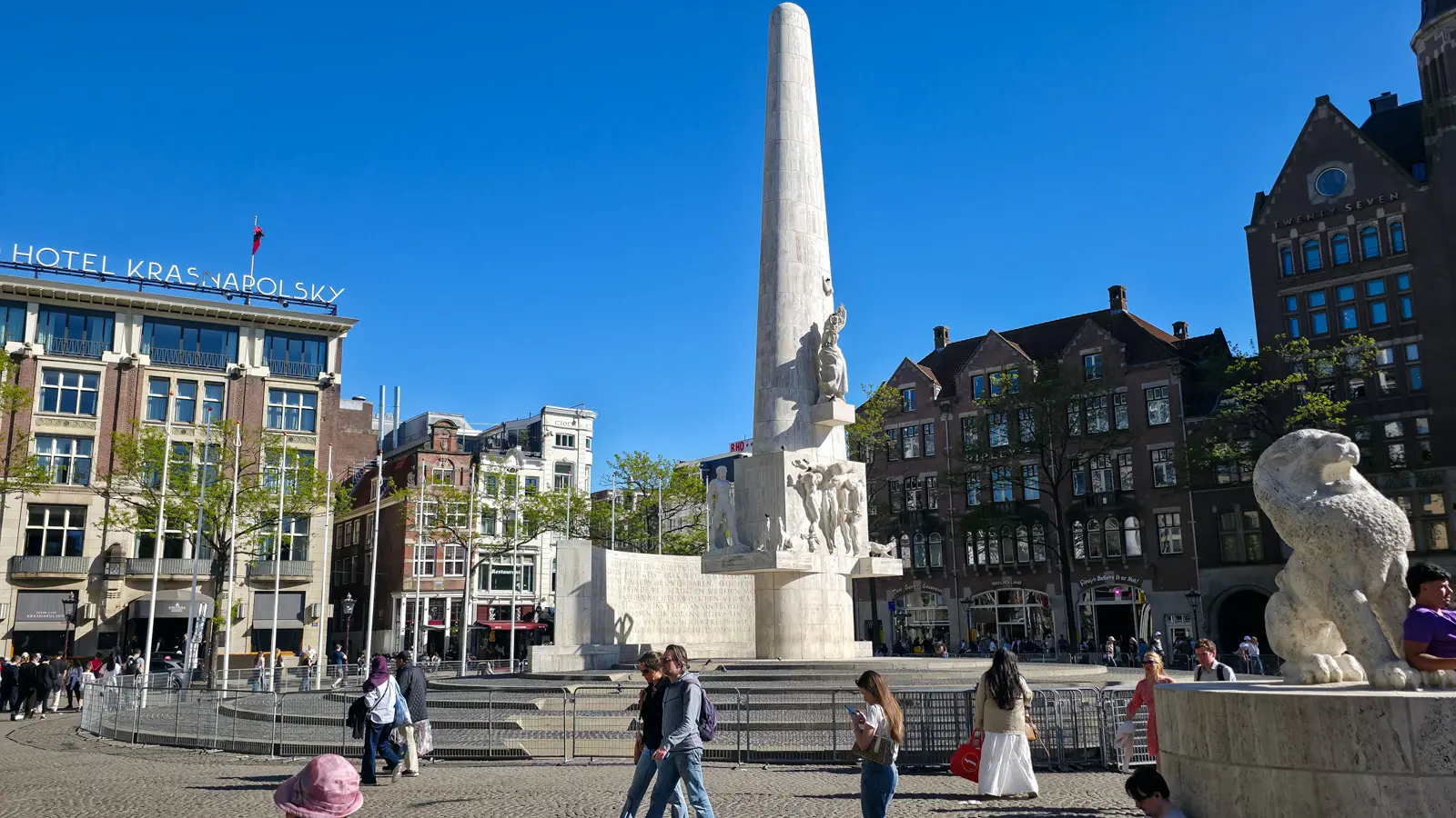 The National Monument on Dam Square, Amsterdam, with a stone lion in the foreground and crowd barriers around the base