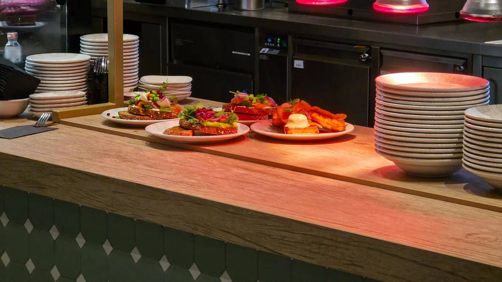 Plates of smoked salmon toast, an avocado toast and a smoked salmon waffle waiting under warming lamps at Café Flor, Schiphol