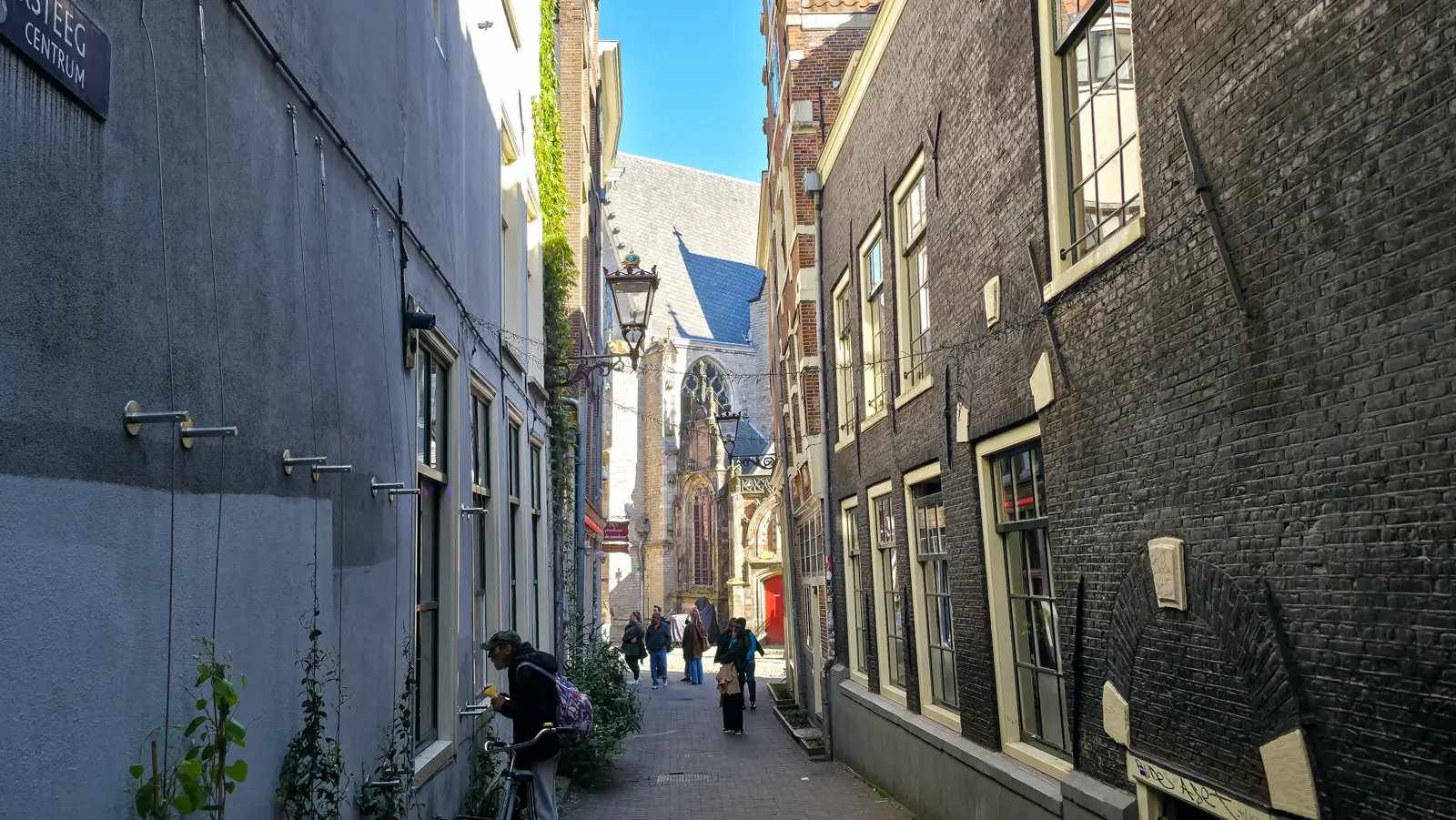 A narrow alley in De Wallen, Amsterdam, leading towards the Gothic stonework and red door of the Oude Kerk
