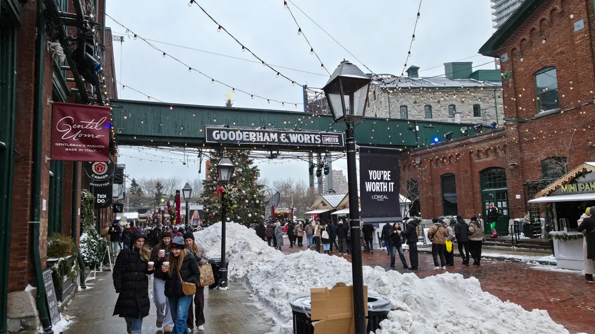 The green Gooderham & Worts Limited bridge over a Distillery District lane in Toronto, with snowbanks and the Christmas tree behind