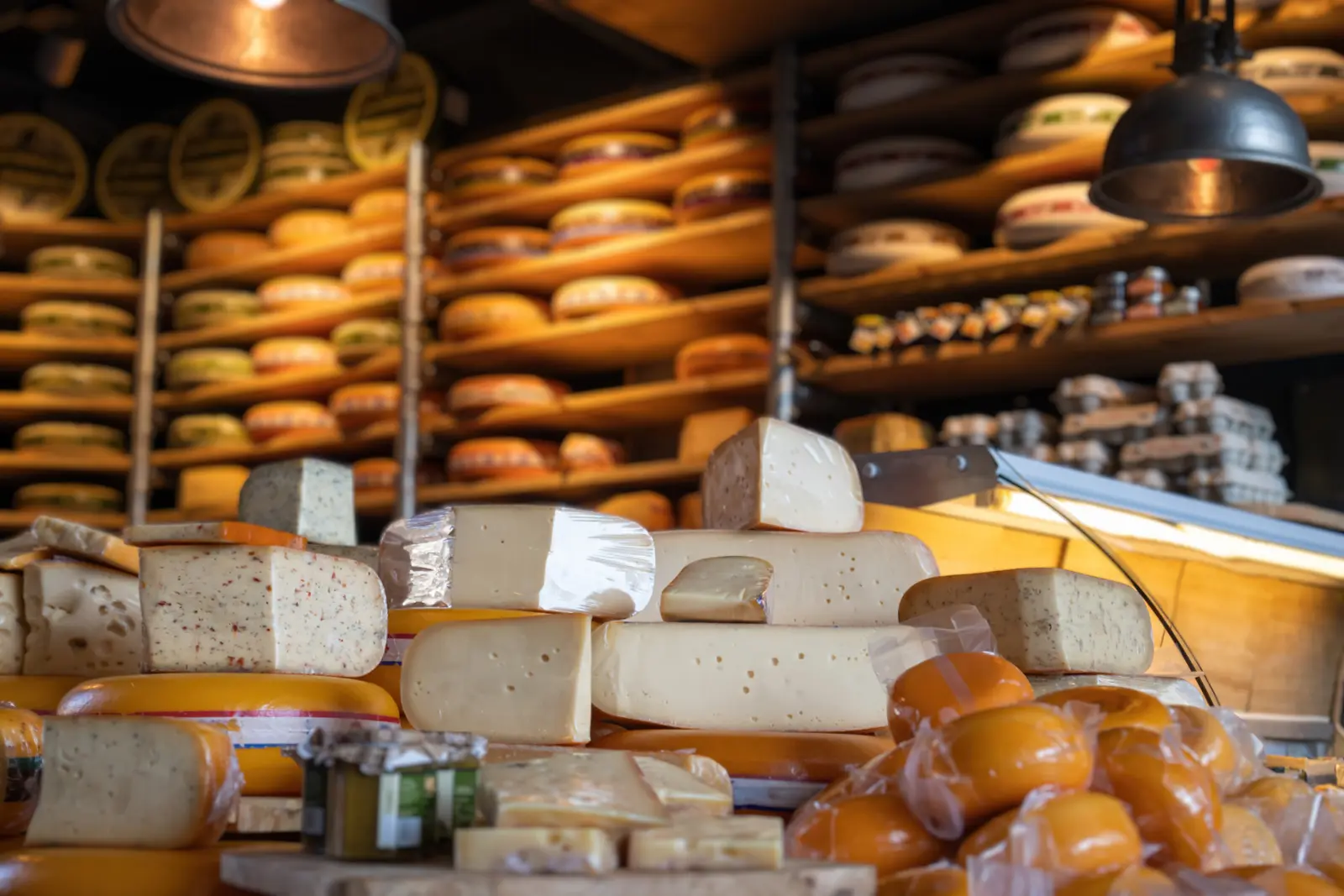 Wheels and wedges of Dutch cheese stacked on the counter and shelves of a cheese shop in Edam