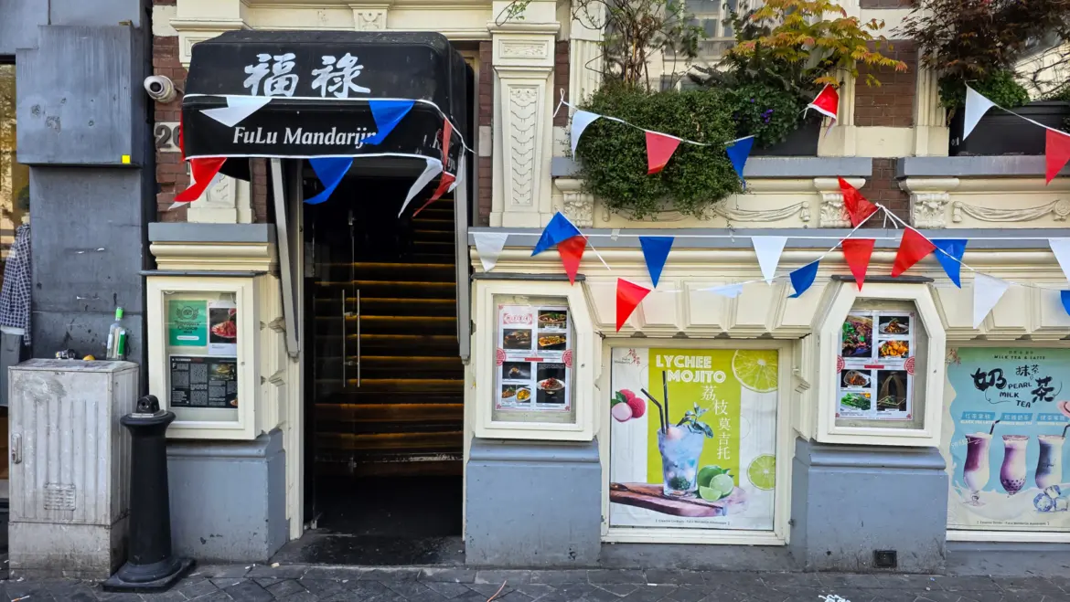 The street entrance of FuLu Mandarijn at Rokin 26, Amsterdam, a narrow glass door under a black awning, hung with red, white and blue bunting