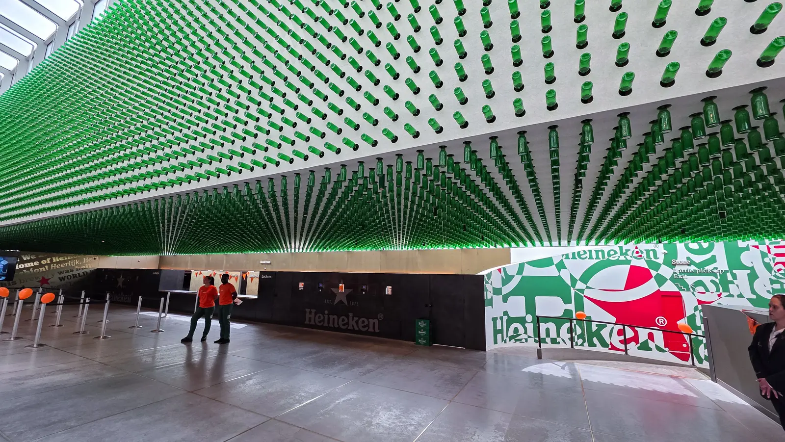 The Heineken Experience entrance hall with hundreds of green bottles on the ceiling and staff in orange shirts
