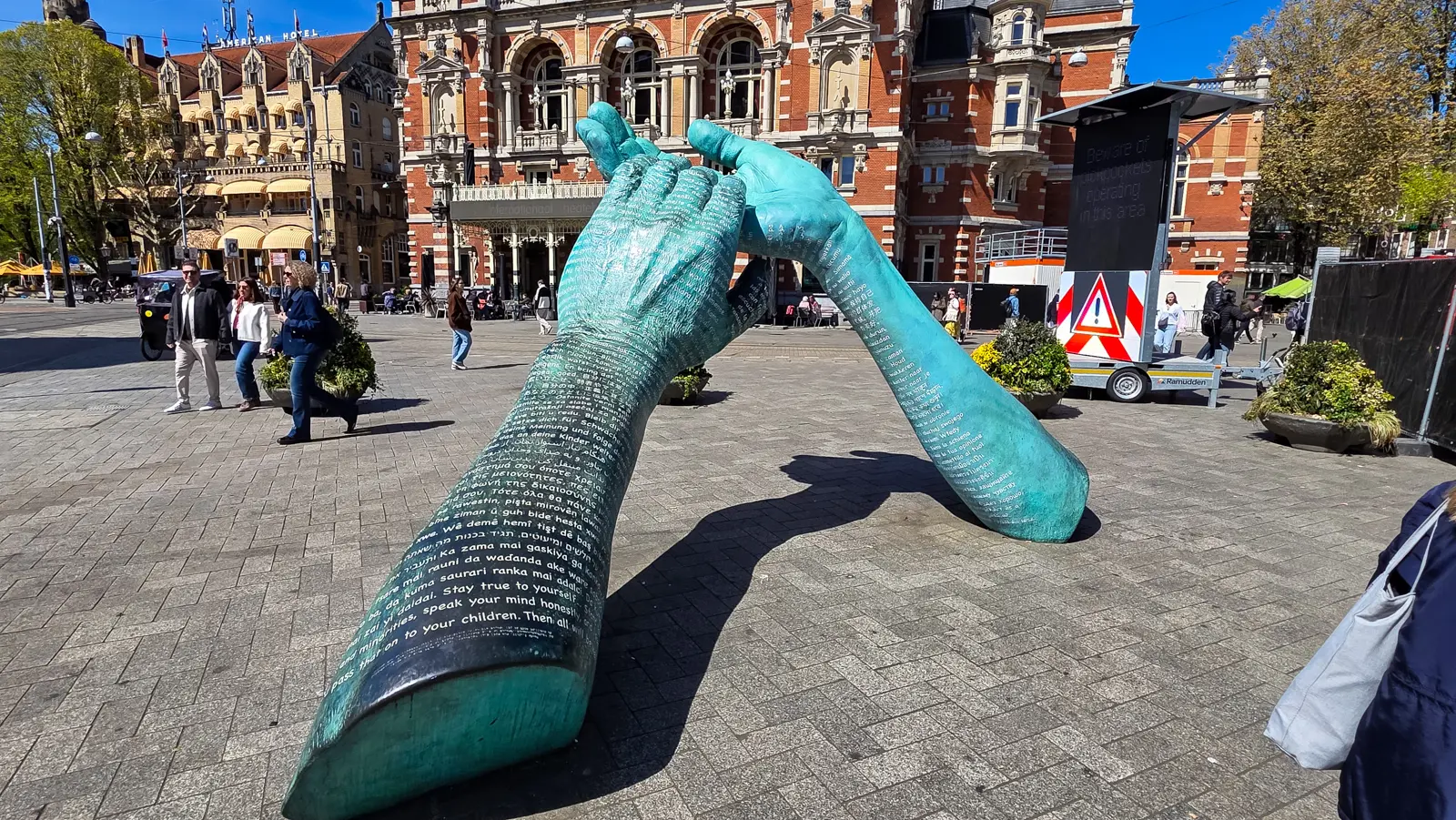 Giant bronze hands covered in text in many languages on the Leidseplein, with the Stadsschouwburg (International Theater Amsterdam) behind, Amsterdam