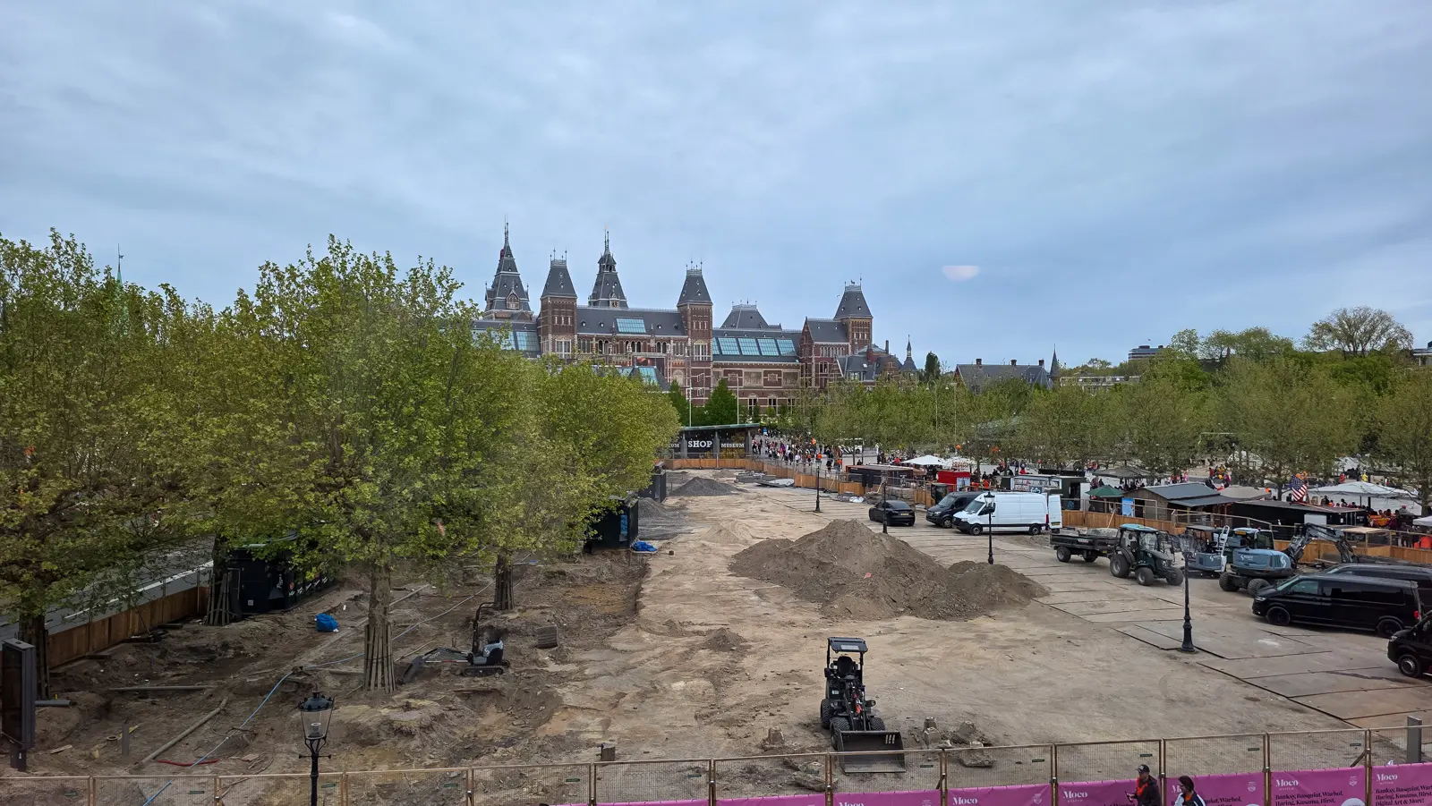 A construction site on Museumplein seen from above, with diggers, sand mounds and the Rijksmuseum behind the trees