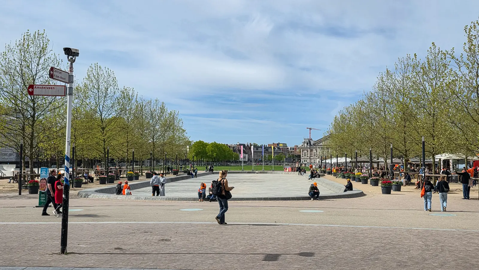The drained pond on Museumplein, Amsterdam, on King's Day, with people in orange and tubs of tulips along the sides