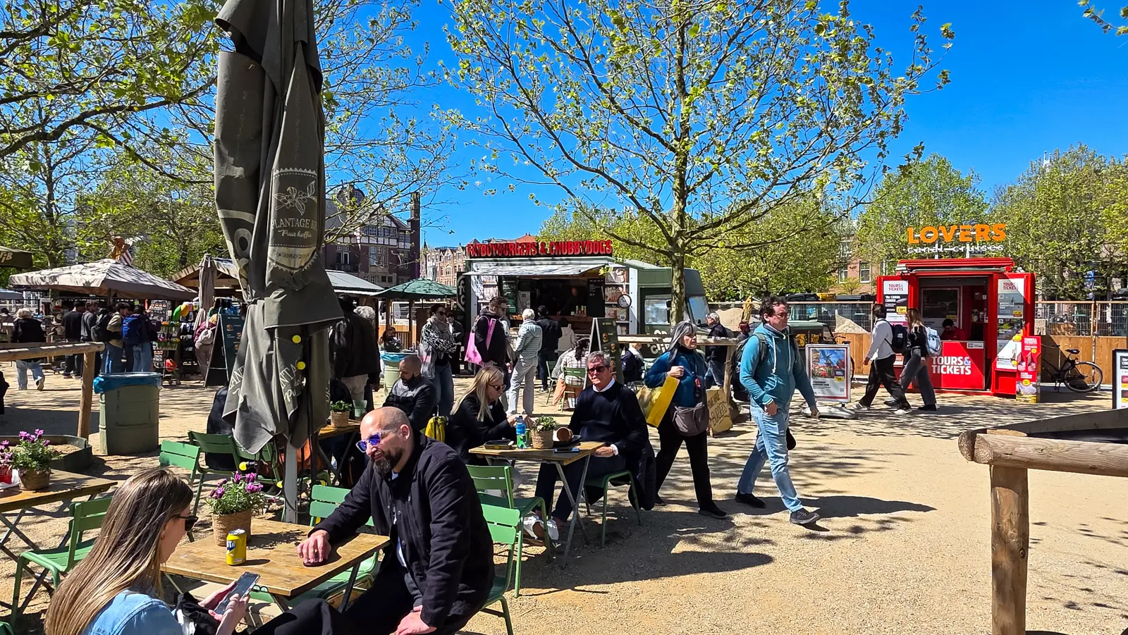 Food trucks, kiosks and green café chairs on the gravel paths of Museumplein, with people eating in the sun