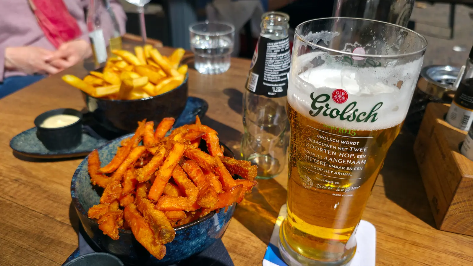 Sweet potato fries and regular fries in blue glazed bowls beside a Grolsch at 't Nieuwe Kafe, Amsterdam