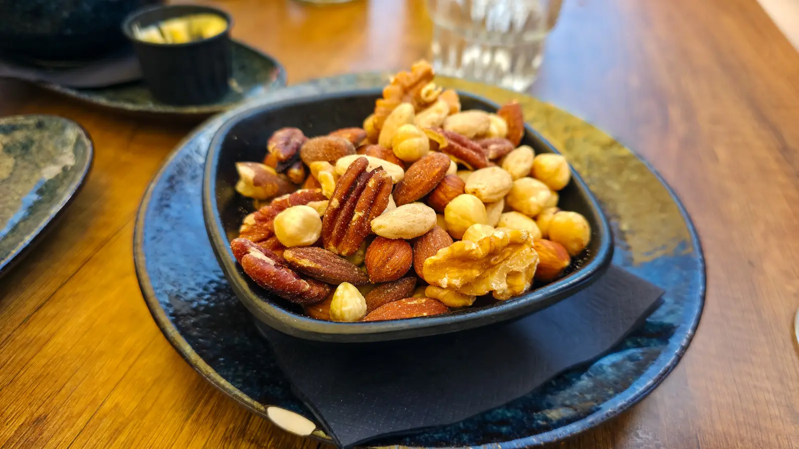 A bowl of mixed almonds, pecans, walnuts and hazelnuts on a blue glazed plate at 't Nieuwe Kafe