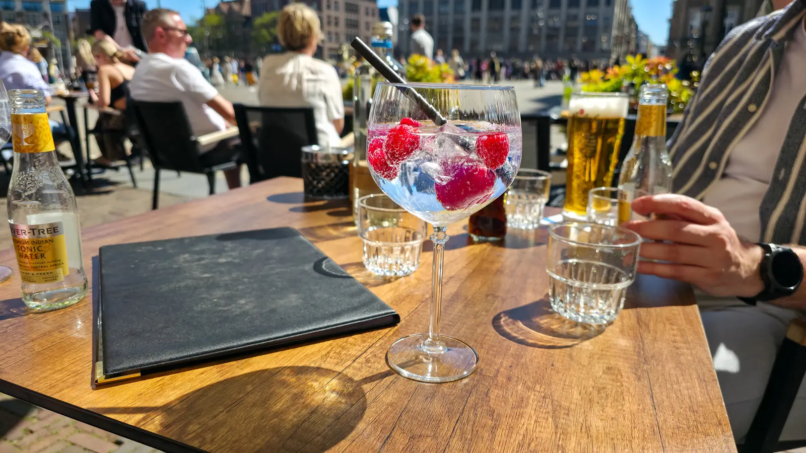 A raspberry gin and tonic in a balloon glass on the terrace at 't Nieuwe Kafe, with Dam Square crowds behind