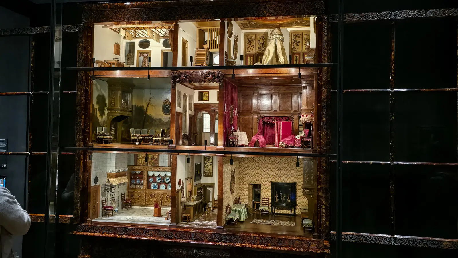 An angled view into Petronella Oortman's dolls' house, a tiled kitchen below and a red bedroom and painted salon above, Rijksmuseum