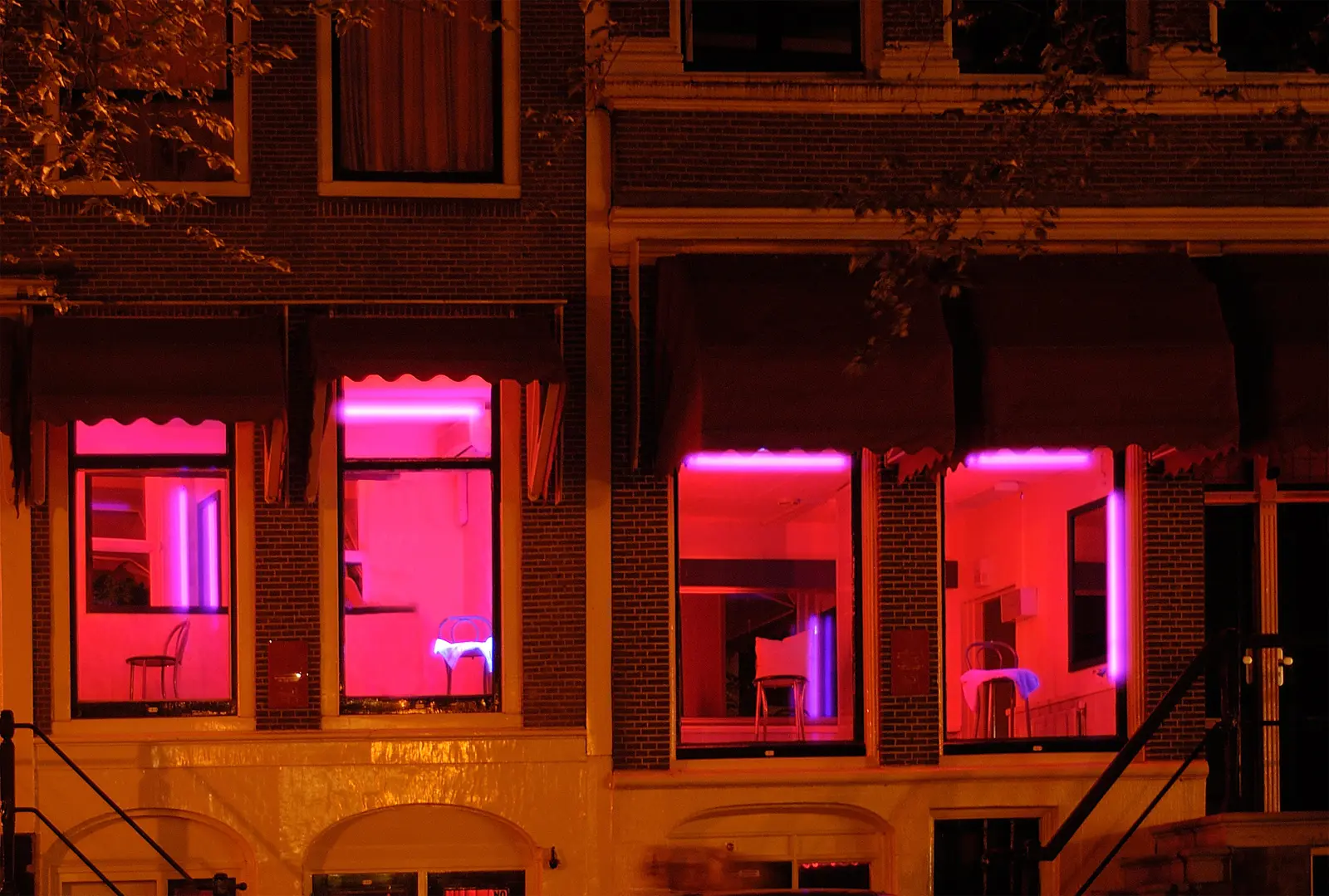 Red-lit windows with empty chairs and pink neon in a row of houses in Amsterdam's Red Light District at night