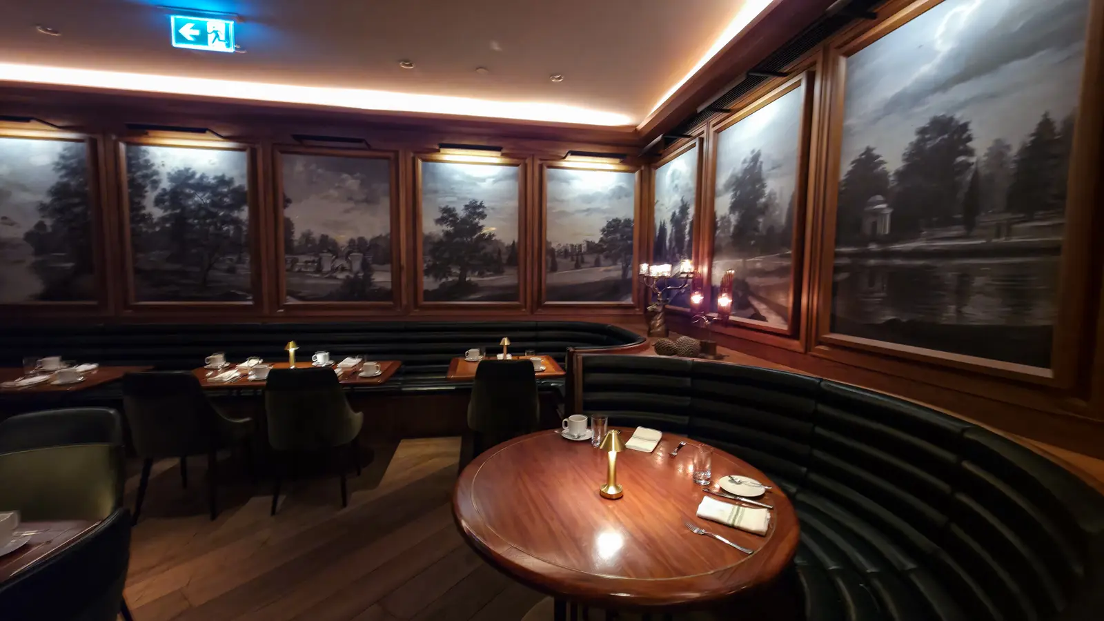 Curved green banquette and round wooden table beneath framed landscape murals, Reign restaurant, Fairmont Royal York