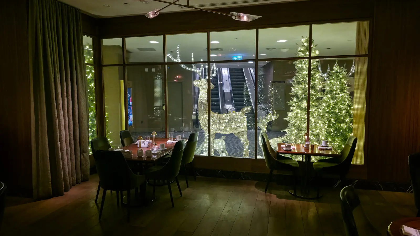 Dining tables set beside a window framing lit reindeer and Christmas trees, Reign restaurant, Fairmont Royal York, Toronto