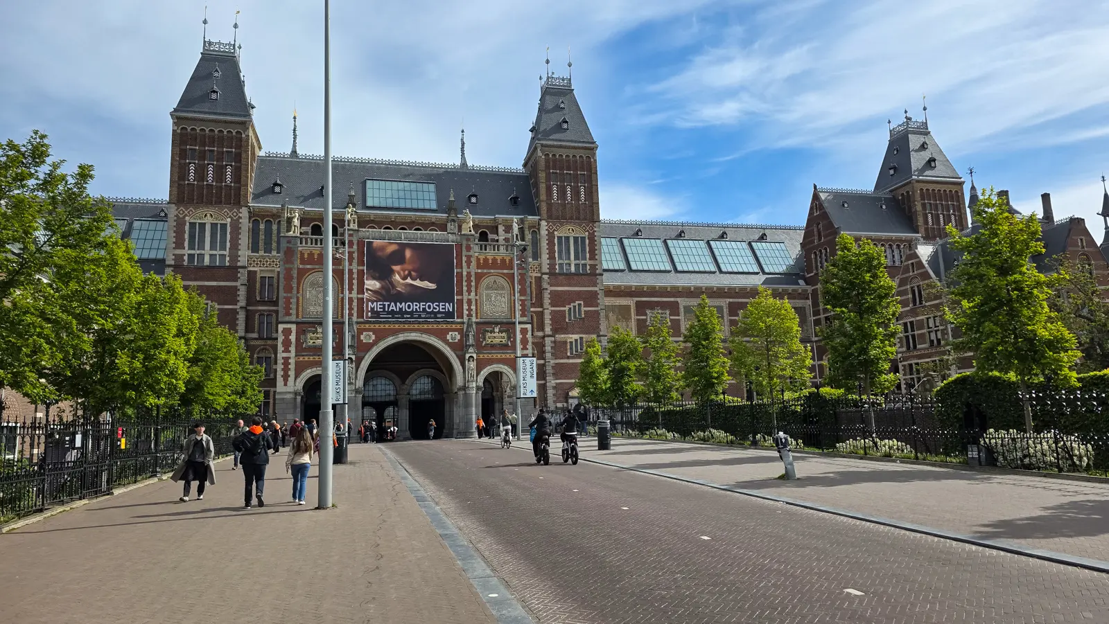 The Rijksmuseum's red-brick front with a Metamorfosen banner, and the public cycle-and-foot passage running under the middle of the building, Amsterdam