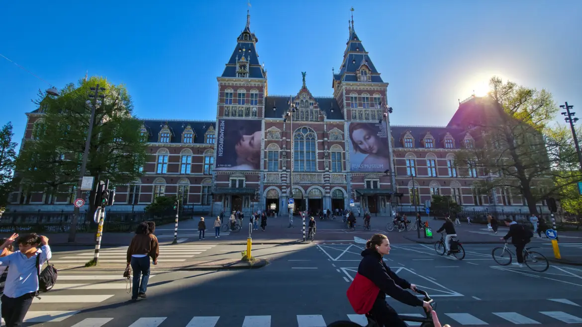 The Rijksmuseum's red-brick front on a spring evening, cyclists crossing in front and the public passage running under the building, Amsterdam