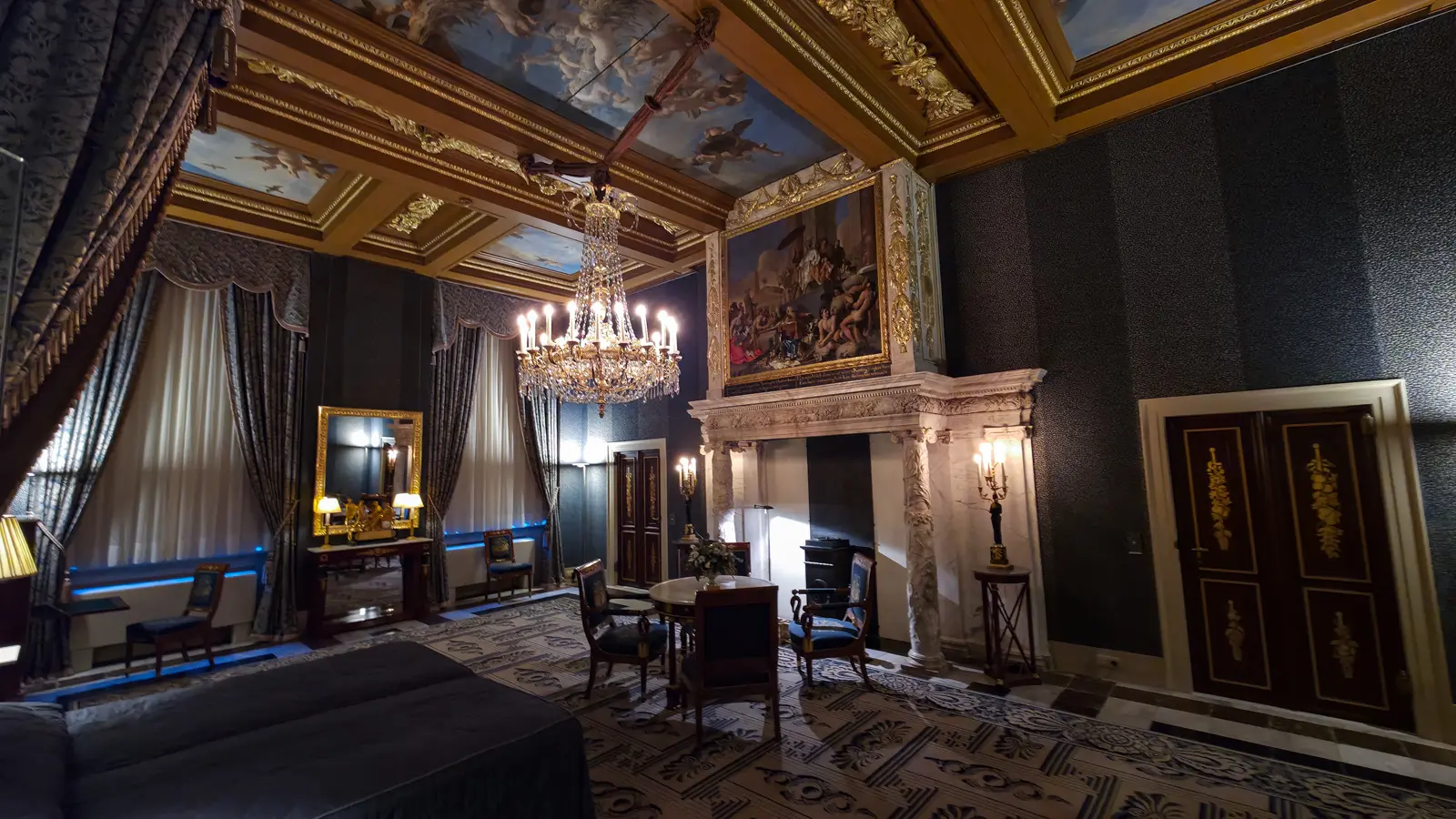 A blue bedroom in the Royal Palace Amsterdam with painted ceiling panels, a crystal chandelier and a marble chimneypiece