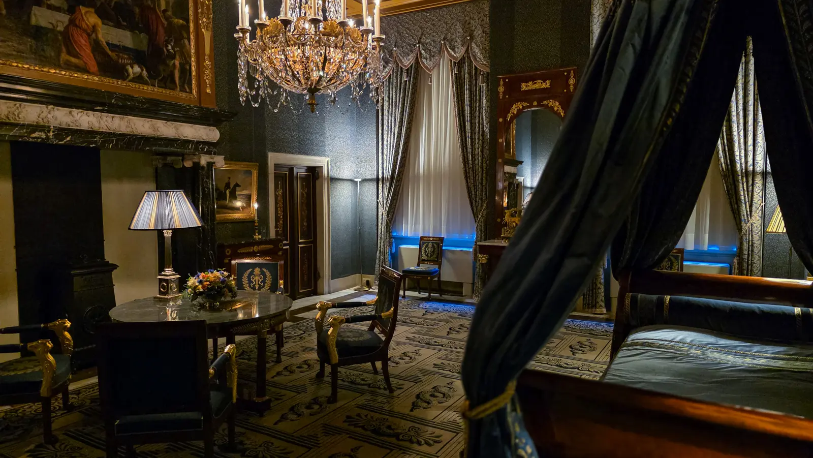A second bedroom with a dark blue canopied bed, Empire armchairs and a black marble fireplace in the Royal Palace Amsterdam