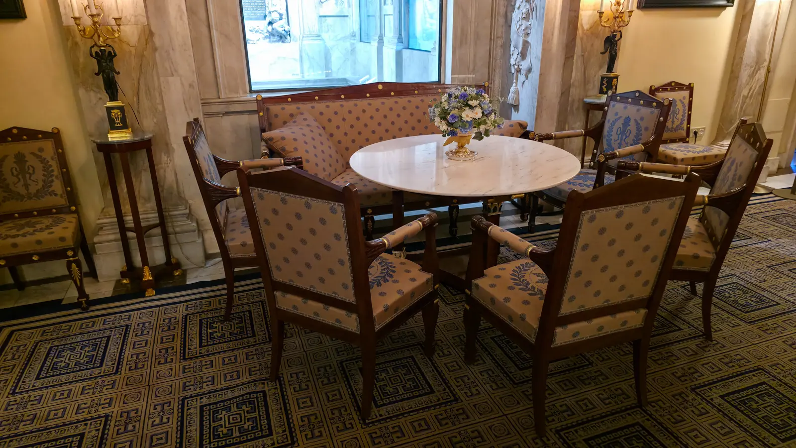 A blue and gold settee and armchairs around a white marble table in the Royal Palace Amsterdam, with a window behind