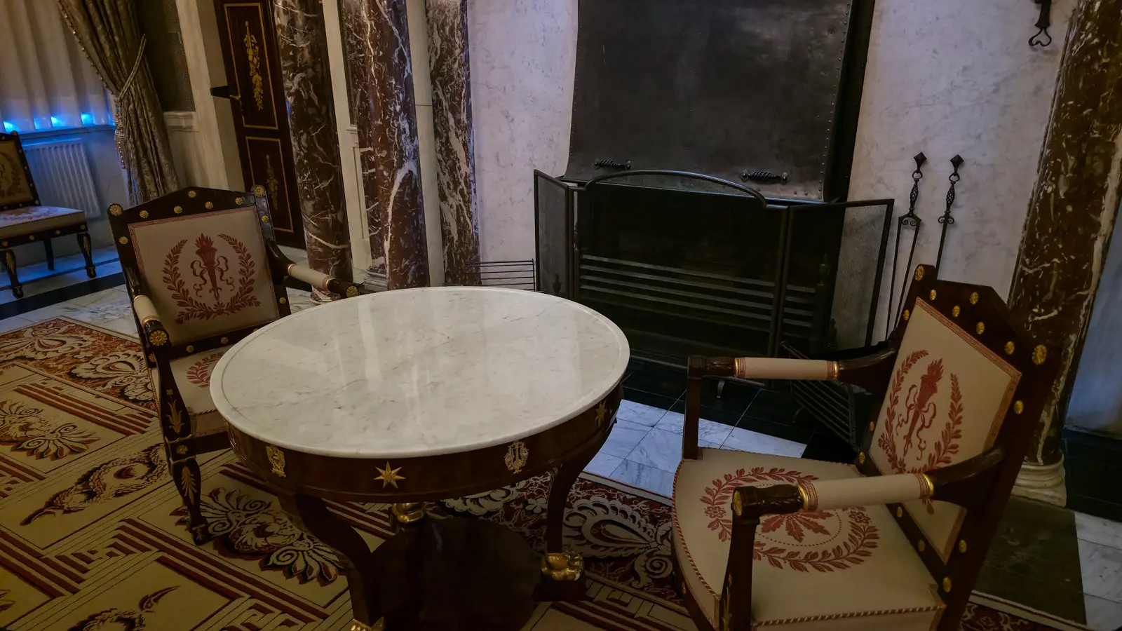 A marble-topped round table and two armchairs embroidered with torches and laurel wreaths, beside a fireplace in the Royal Palace Amsterdam