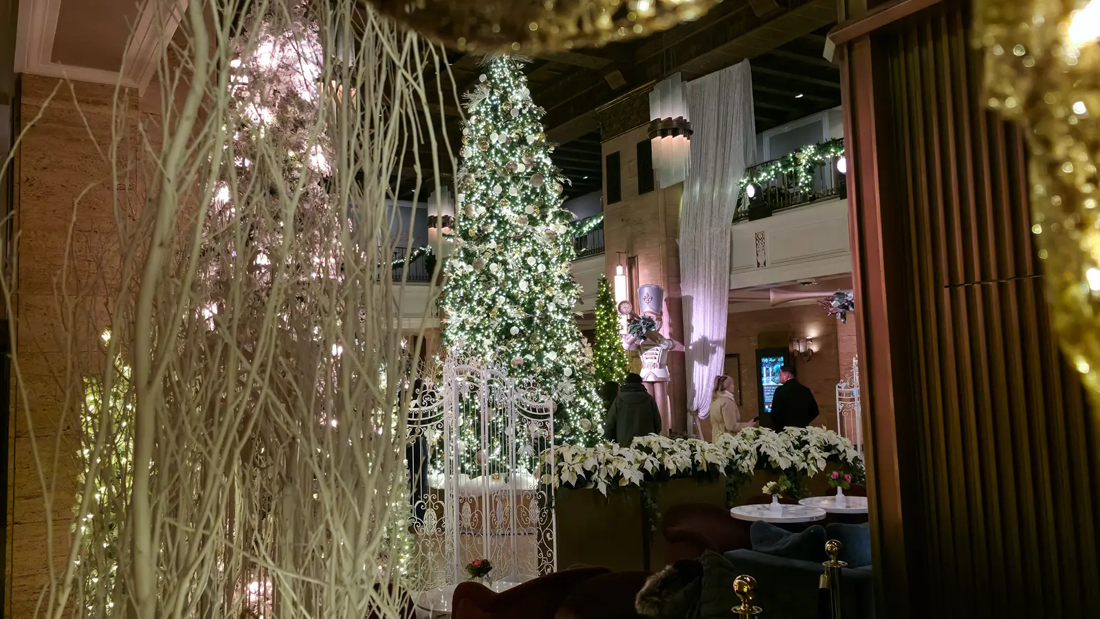 The Fairmont Royal York's Christmas tree seen from the lobby floor through white branches, with white gates and poinsettias