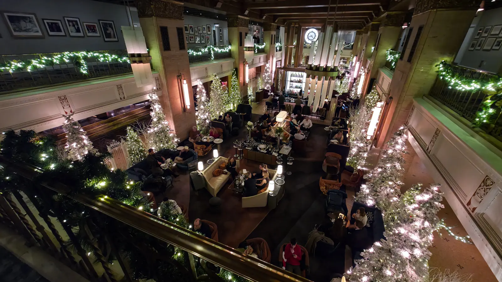 The Fairmont Royal York's Clockwork lounge seen from the balcony, filled with guests and framed by frosted Christmas trees